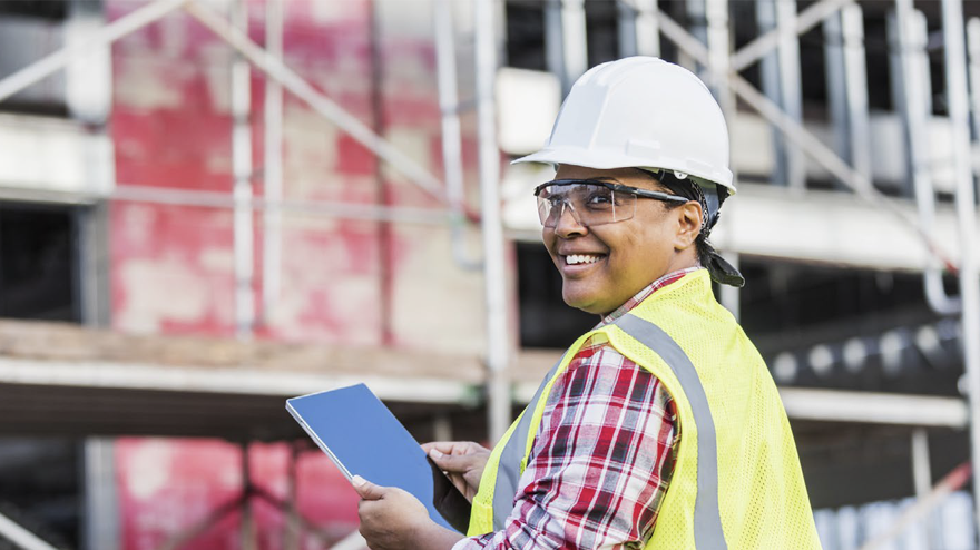 A woman wearing a hardhat and safety glasses holding a tablet