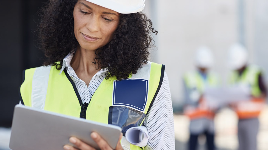 A woman wearing a safety vest looking at a tablet