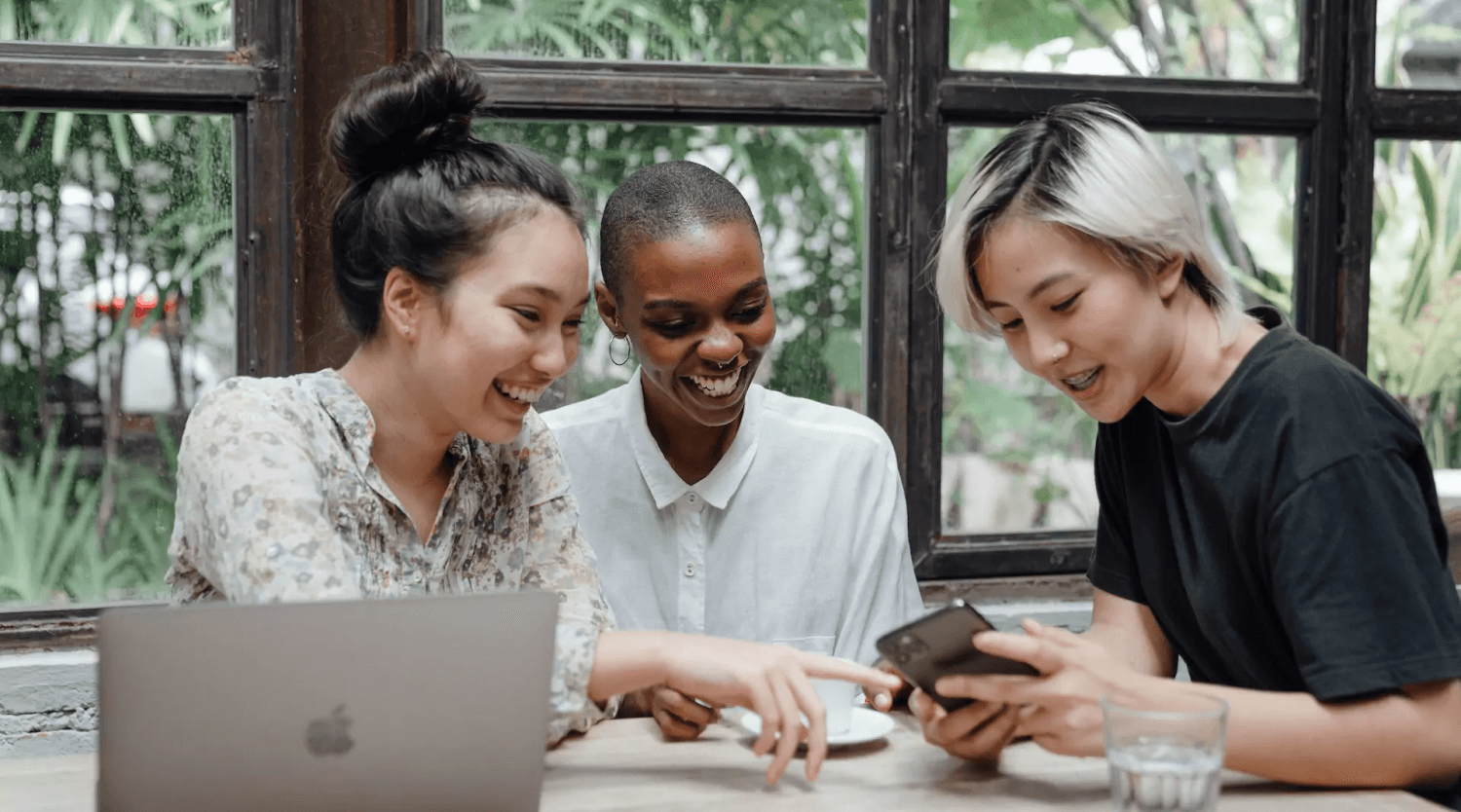 Group of friends sitting at a table looking at one person's mobile phone