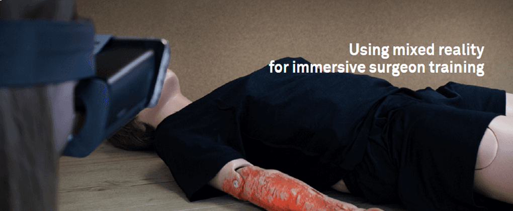 Banner zum Projekt „Ember“, das eine Person mit einem VR-Headset zeigt, die eine medizinische Puppe mit einer simulierten Verbrennung am ARM betrachtet – für ein immersives Chirurgentraining.