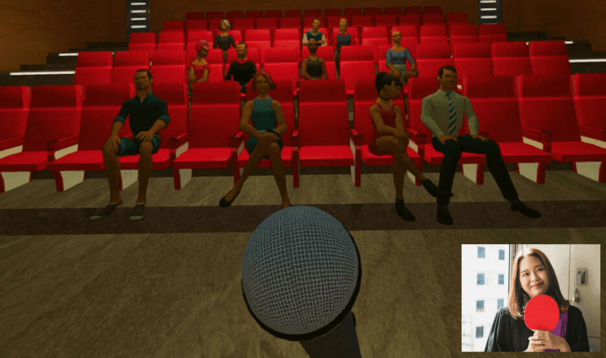 A theater with red seats, occupied by several people seated, a microphone in the foreground, and a photo of a person holding a ping pong paddle inset in the bottom right.