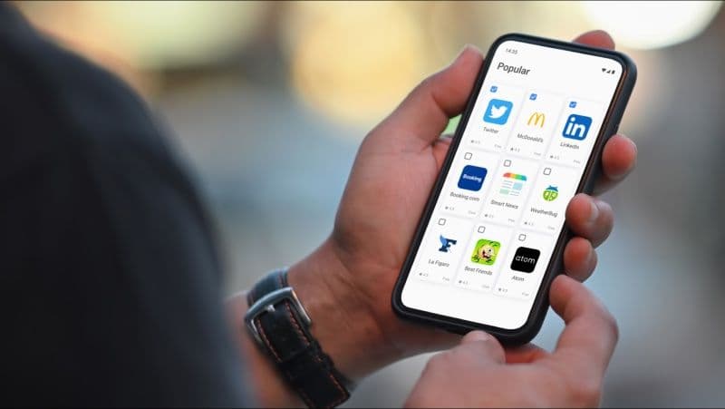 画面に9つのアプリが表示された携帯電話を持つ人物