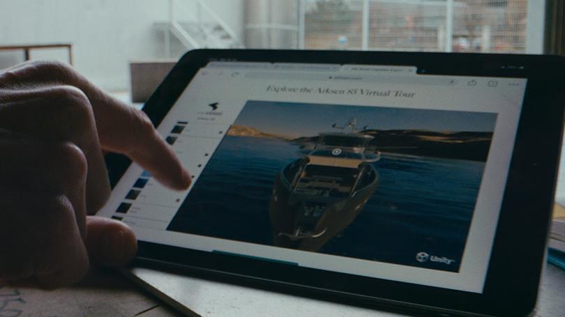 Mão apontando para um iPad onde um barco é exibido